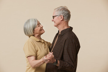 Minimal waist up portrait of happy senior couple dancing and looking at each other against beige background