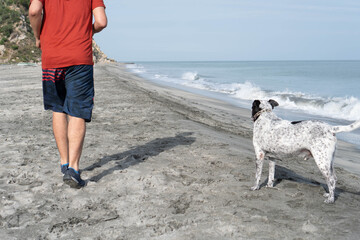 Latin Man having fun with his dog on the beach in the morning