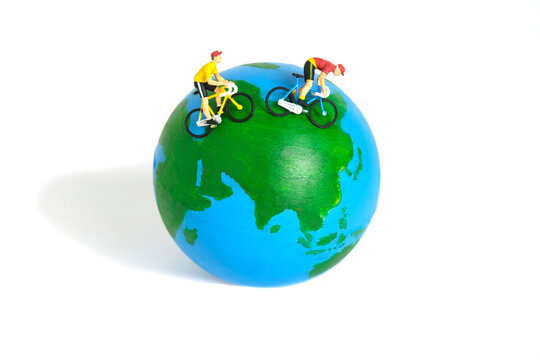 Miniature people toy figure photography. World bicycle day or tour around the world concept. A biker cycling above earth globe, isolated on white background.