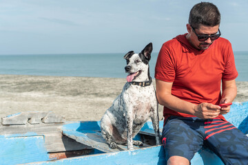 Man checking his cell phone with his dog on the beach in summertime