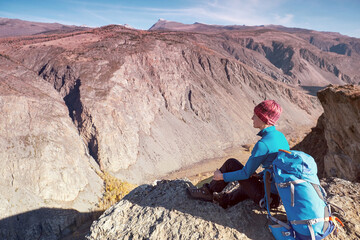 Fototapeta premium Hiker woman with backpack sitting on rock of a mountain