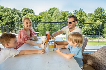 Happy family sitting and drinking, celebrating, toasting, in outdoor hotel cafe bar