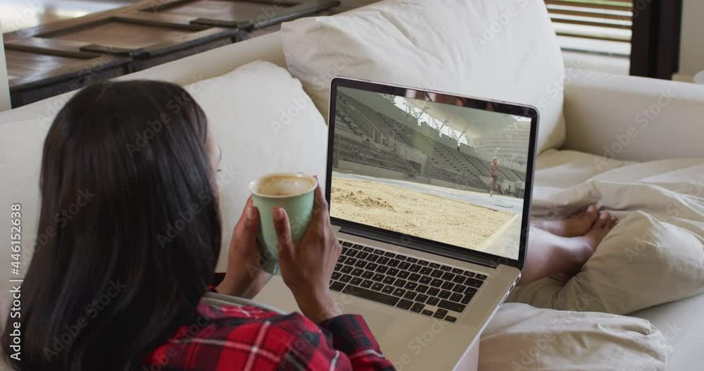 Sticker Composite of woman sitting at home holding coffee watching athletics long jump event on laptop