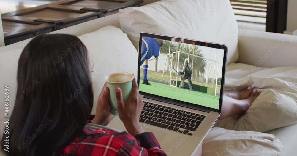 Canvas Prints Composite of woman sitting at home holding coffee watching hockey match on laptop