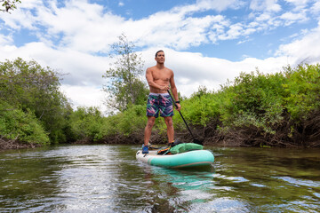 Adventurous Hispanic Adult Athletic Man paddle boarding on The River of Golden Dreams. Located in...