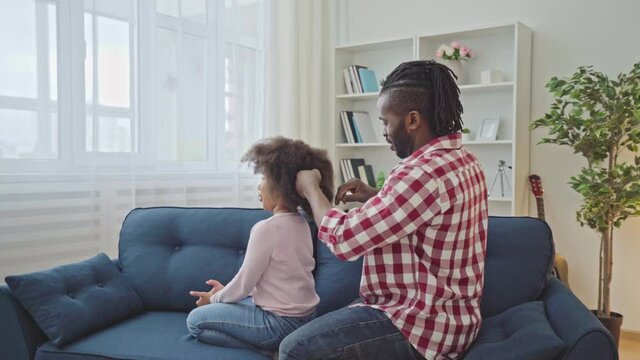 Young black father combing natural afro hair of daughter, making hairstyle