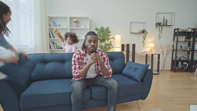 Stressed single father sitting on sofa while daughters having fun, parenting