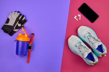 Concept of fitness, sports and diet, top view, flat lay. Fitness equipment on a purple-pink background. Athlete set of sneakers, mobile phone, headphones, smart watch, shaker bottle and sports gloves