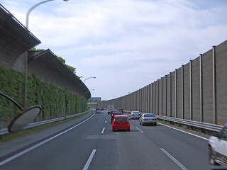 Entering Tokyo by highway with tall green Overgrown noise barriers with grass on roadsides, distant downtown Office buildings in background, Japan