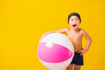 Summer vacation concept, Portrait Asian happy cute little child boy smiling in swimsuit hold beach ball, Kid having fun with inflatable ball in summer vacation, studio shot isolated yellow background