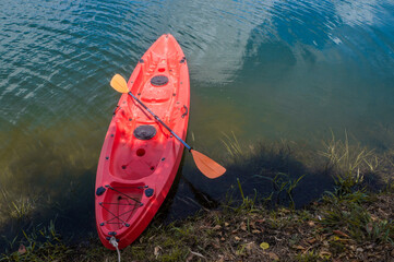 Red kayak with paddle parked by the lake on a sunny day