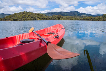 Red kayak with paddle parked by the lake on a sunny day. It's a nice day with blue skies