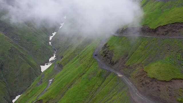 Wide cinematic drone shot of vehicle driving on one of the world's most dangerous roads in Tusheti Georgia, the of the Abano Pass, with clouds in the foreground