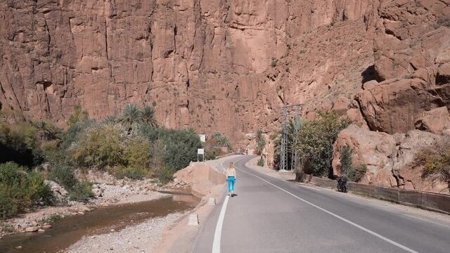 Scenic view of rocky canyon cliff with girl walking on highway at Todra Gorges
