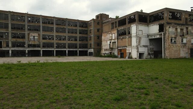 Drone flyover, rising forward, over a crumbling abandoned furniture factory. Cool and gloomy.