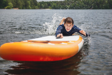 Joyful teenager boy falling into water from his paddle board. Summer fun, sports and activity