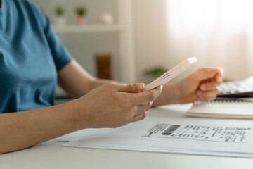 A woman uses a smartphone to scan the barcode to pay monthly phone bills after receiving an invoice...