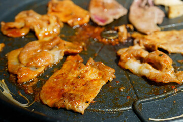 Sliced raw pork into thin slices is placed on a black grill to cook before eating.