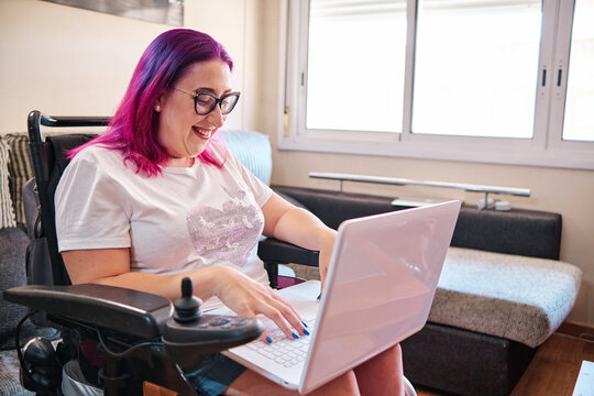 adult woman with disabilites in a wheelchair working at home with laptop