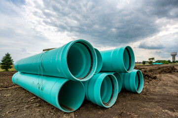 Stacked water main pipe with bell fitting next to an exposed trench for installation