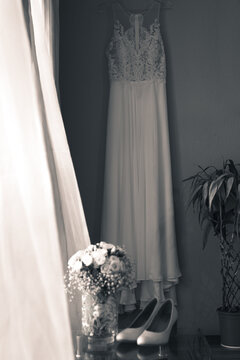 vertical shot of wedding rings by the window with blowing curtains and some slippers and a white flower arrangement on a glass table