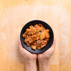 Korean food, Stir-fried kimchi cabbage with pork on dish holding by hand, Table top view