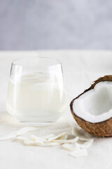 Coconut water or milk in a glass, coconut chips and half of a fresh and juicy coconut lie next to it. Vegetarian snack, healthy snack. Vertical photo
