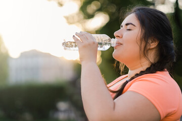 Dehydrated woman. Water thirst. Nutrition wellness. Body healthcare. Side view portrait of obese overweight drinking lady in defocused copy space sunset background.