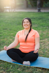 Yoga practicing. Harmony balance. Mind freedom. Body positive. Relaxed happy overweight obese woman in lotus pose enjoying green nature in spring park landscape.