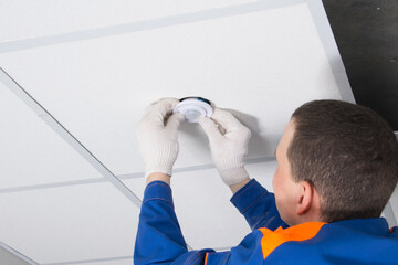 close-up of the installation of a motion sensor for lighting automation, with hands in protective gloves of an electrician