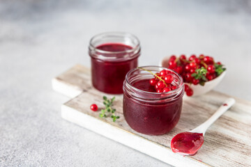Homemade red currant jam or jelly in glass jars and red currants fresh berries on wooden cutting board.