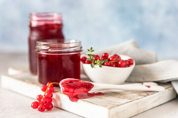 Homemade red currant jam or jelly in glass jars and red currants fresh berries on wooden cutting board.