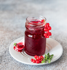 Glass jar with red currant jelly or jam and fresh red currant berries.