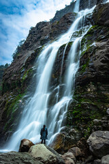 Fototapeta premium waterfall white water stream falling from mountains with girl standing nearby at day long exposure