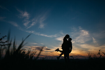 silhouette of a couple at sunset. guy holding a girl in his arms.