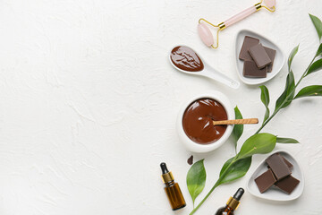 Composition with bottles of essential oil, facial massage tool and melted chocolate on light background