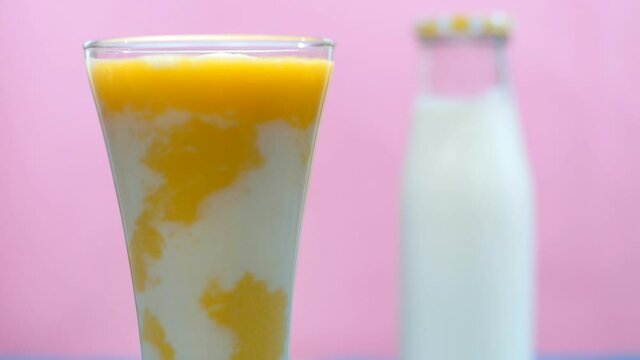 Refreshing mango milkshake kept on a wooden table - nutritious breakfast. Closeup shot of a fresh bottle of milk and glass of healthy vegan Aam Lassi kept together against a colored background
