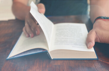Naklejka premium Close-up of a man sitting at a wooden table and reading a book