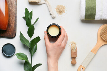 Female hand with jar of cosmetic product and bath supplies on light background
