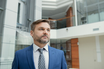 Mature bearded businessman in suit looking away while standing at office and waiting for somebody