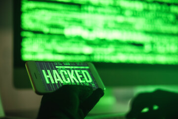 Hacker with mobile phone using computer in dark room