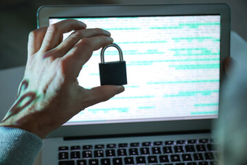 Hand of hacker with padlock near screen of laptop