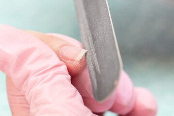 Manicurist filing client's nails at table, closeup. Woman in nail salon receiving manicure by beautician. Manicure process in beauty salon, close up. Shallow depth of field