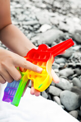 A child plays a multi-colored colorful pop it in the shape of a unicorn on a sea pebble beach against the background of a white terry towel. Popit in the hands of a child.