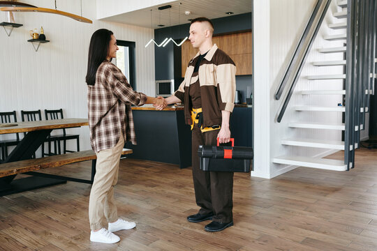 Female client shaking hand of repairman with toolbox after making service