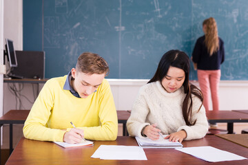Two teenage students Chinese girl and European guy studying together in schoolroom. Education concept