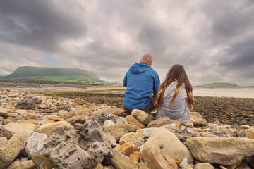 Father and daughter sitting on a rocks of Strandhill beach and enjoy view on Knocknarea mountain