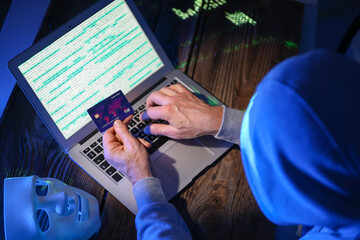 Hacker with credit card using computer in dark room