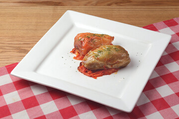 Stuffed paprika pepper with meat, rice and vegetables served on a white plate over red plaid tablecloth.