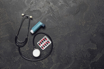 Modern inhaler, pills and stethoscope on dark background